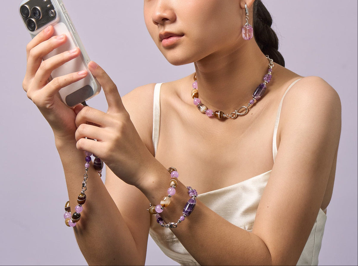The Violet Chocolate worn as a necklace and bracelet while holding a phone, the charm hanging from the case